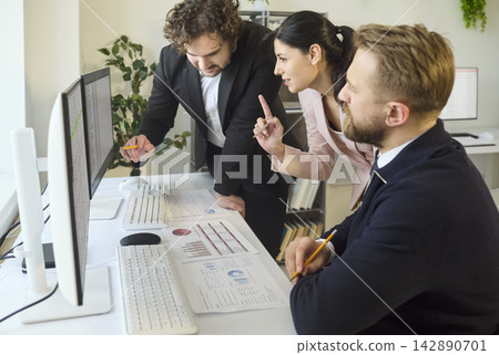 Team of coworkers analyzing charts on computer screens during office meeting Team of coworkers analyzing charts on computer screens during office meeting 142890701