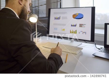 Businessman reviewing charts on desktop monitor, planning strategy at office desk Businessman reviewing charts on desktop monitor, planning strategy at office desk 142890741