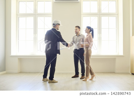 Couple discussing real estate with contractor, handshake in empty bright apartment Couple discussing real estate with contractor, handshake in empty bright apartment 142890743