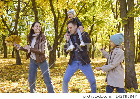 Happy family with two children playing among yellow autumn leaves in a sunny park Happy family with two children playing among yellow autumn leaves in a sunny park 142890847