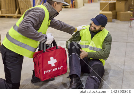 Coworker aids injured warehouse worker using first aid kit during safety response Coworker aids injured warehouse worker using first aid kit during safety response 142890868