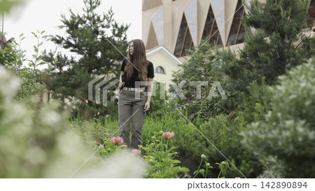 Young woman with backpack pauses in urban garden beside blooming peonies, modern glass architecture, soft daylight, calm pose, turned gaze, layered greenery, refined city landscape Young woman with backpack pauses in urban garden beside blooming peonies, modern glass architecture, soft daylight, calm pose, turned gaze, layered greenery, refined city landscape 142890894