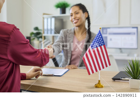 Immigration consultant handshake with client after visa approval, USA flag on desk Immigration consultant handshake with client after visa approval, USA flag on desk 142890911