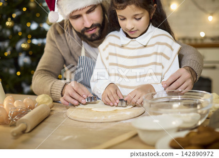 Father guiding daughter cut shapes dough for Christmas cookies in cozy home kitchen 142890972