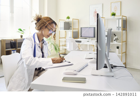 Female doctor at computer updating patient records in modern clinic office Female doctor at computer updating patient records in modern clinic office 142891011