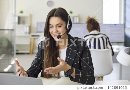 Female call center agent with headset on laptop video chat in modern office Female call center agent with headset on laptop video chat in modern office 142891013
