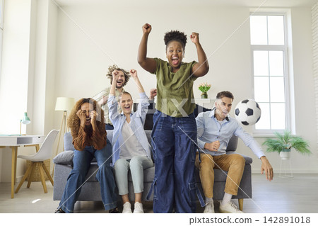 Friends cheer soccer goal at home, celebrating while watching on television Friends cheer soccer goal at home, celebrating while watching on television 142891018
