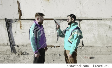 Confrontation Against Urban Backdrop. Urban Scene With Confrontational Men And Vibrant Fashion Contrast . Media 142891030