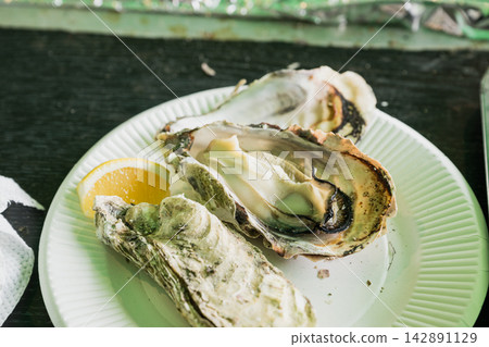 A close-up of delicious-looking grilled oysters on a plate with lemon (Sea Milk Gourmet) 142891129
