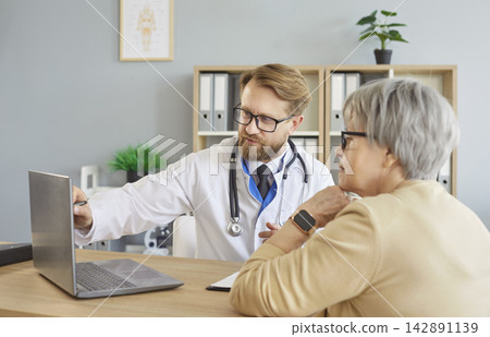 Doctor Consulting Elderly Patient With Laptop 142891139