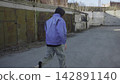 Back view person in blue jacket walking through industrial yard beside metal containers under muted daylight, with person, walking, blue, jacket detail, showing industrial, yard, container, metal 142891140