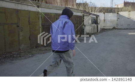 Back view person in blue jacket walking through industrial yard beside metal containers under muted daylight, with person, walking, blue, jacket detail, showing industrial, yard, container, metal Back view person in blue jacket walking through industrial yard beside metal containers under muted daylight, with person, walking, blue, jacket detail, showing industrial, yard, container, metal 142891140