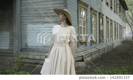 Woman in Light Dress Standing by Old Wooden House Woman in Light Dress Standing by Old Wooden House 142891157