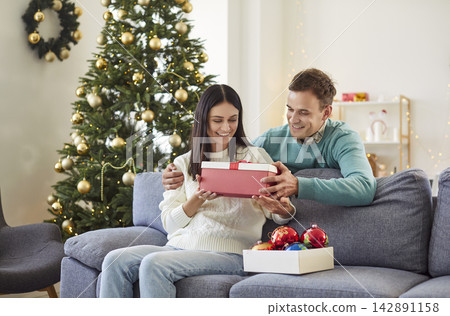 Husband Giving A Gift To Wife During New Year Or Christmas Celebration At Home 142891158