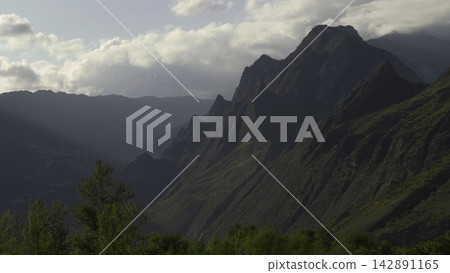 Dramatic Shadows Over Rugged Mountain Terrain. Aerial Shot Highlighting Deep Valleys And Lush Foliage. Creative Dramatic Shadows Over Rugged Mountain Terrain. Aerial Shot Highlighting Deep Valleys And Lush Foliage. Creative 142891165