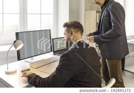 Business finance analysts reviewing data reports at office computer workstations Business finance analysts reviewing data reports at office computer workstations 142891272