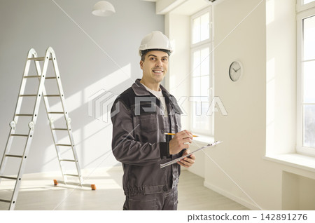 Smiling construction worker with hard hat and clipboard in bright interior Smiling construction worker with hard hat and clipboard in bright interior 142891276