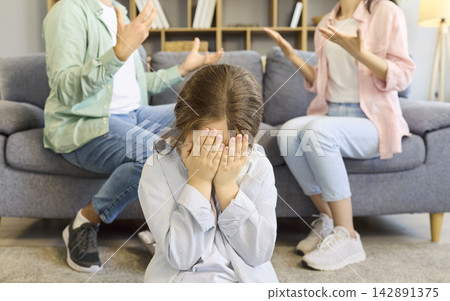 Upset child covering face as parents argue, family conflict and emotional stress Upset child covering face as parents argue, family conflict and emotional stress 142891375