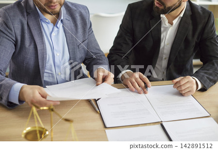Legal client and lawyer reviewing contract before signing, scales of justice on table Legal client and lawyer reviewing contract before signing, scales of justice on table 142891512