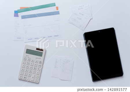 一張擺放著平板電腦、計算機、收據和發票的報稅和會計工作場景圖片。 一張擺放著平板電腦、計算機、收據和發票的報稅和會計工作場景圖片。 142891577
