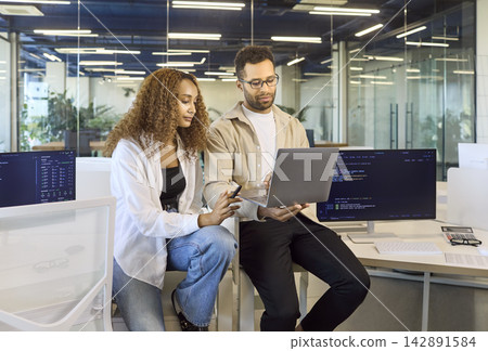 Coworkers collaborating on laptop in modern office, reviewing code and insights Coworkers collaborating on laptop in modern office, reviewing code and insights 142891584