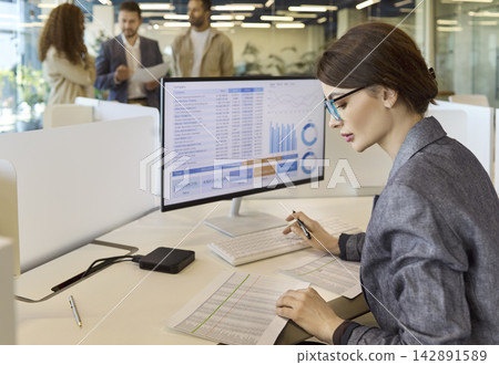 Businesswoman financial analyst reviewing spreadsheets and charts at office desk Businesswoman financial analyst reviewing spreadsheets and charts at office desk 142891589