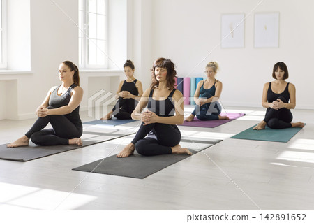 Womens yoga class warming up on mats in bright studio with calm, focused energy 142891652