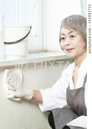 A senior woman wiping down surfaces in the living room. 142891715