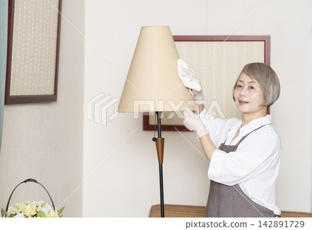 一位老婦人正在擦拭客廳裡的各種表面。 一位老婦人正在擦拭客廳裡的各種表面。 142891729