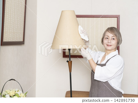 一位老婦人正在擦拭客廳裡的各種表面。 一位老婦人正在擦拭客廳裡的各種表面。 142891730