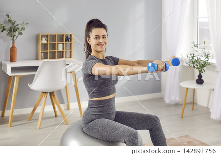 Sporty happy woman losing weight at home and exercising with dumbbells Sporty happy woman losing weight at home and exercising with dumbbells 142891756