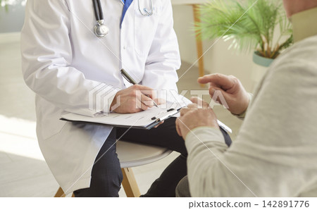 Faceless doctor cardiologist in white coat writing down prescription to old man patient Faceless doctor cardiologist in white coat writing down prescription to old man patient 142891776