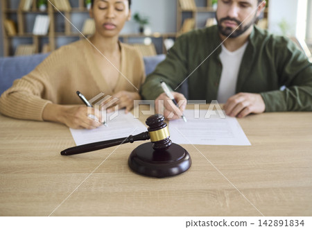 Couple signing divorce documents at desk with court gavel, separation concept 142891834