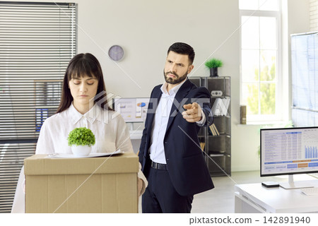 Manager fires employee with box after dismissal in modern office setting Manager fires employee with box after dismissal in modern office setting 142891940
