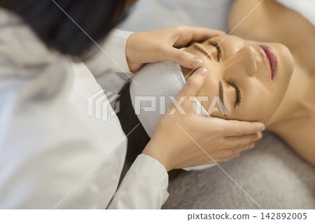 Close up photo of pretty young woman lying with closed eyes and having face or head massage in spa Close up photo of pretty young woman lying with closed eyes and having face or head massage in spa 142892005