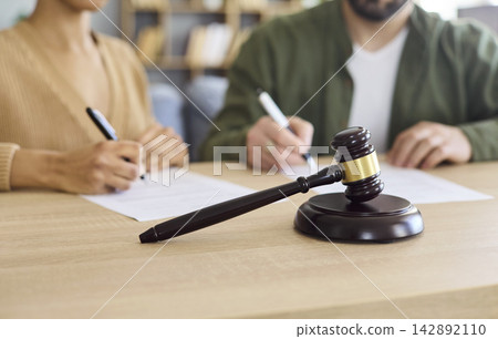 Couple Signing Divorce Papers with Judge Gavel on Desk in Office, Legal Separation 142892110