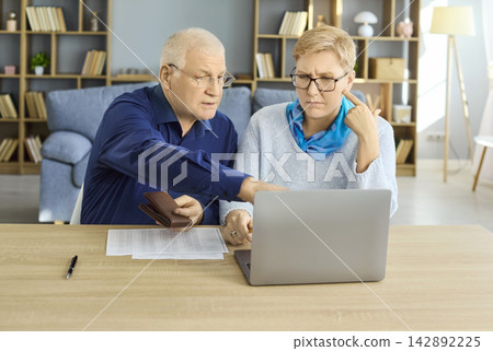 Senior couple reviewing bills and budgeting finances at home with laptop for retirement Senior couple reviewing bills and budgeting finances at home with laptop for retirement 142892225