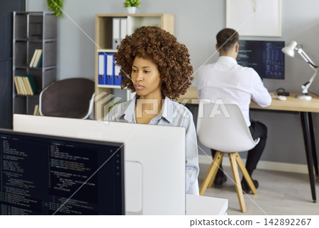 Female software developer coding at desktop in modern office workspace environment Female software developer coding at desktop in modern office workspace environment 142892267