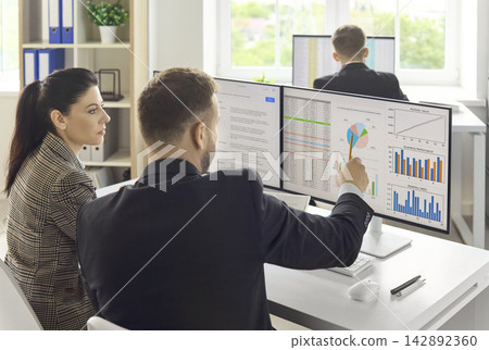 Colleagues discussing market data and strategy charts on computer monitors Colleagues discussing market data and strategy charts on computer monitors 142892360