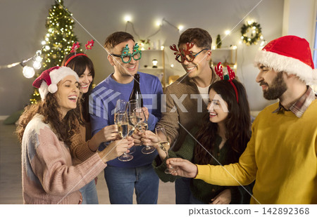 Cheerful friends clink champagne at cozy home Christmas party in Santa hats Cheerful friends clink champagne at cozy home Christmas party in Santa hats 142892368