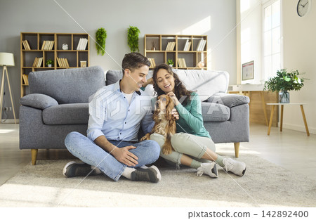 Smiling couple sitting with cocker spaniel dog in cozy bright living room at home 142892400