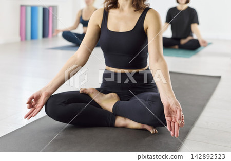 Closeup of woman in lotus pose meditating during yoga class session indoors Closeup of woman in lotus pose meditating during yoga class session indoors 142892523