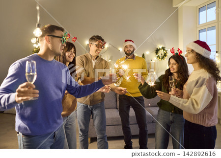 Group of friends lighting sparklers at cozy Christmas home party, laughing together 142892616