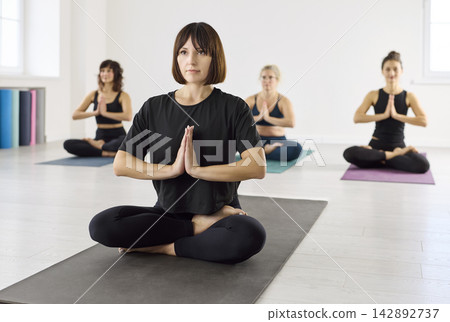 Calm yoga class with women seated in lotus, namaste hands and focused breathing Calm yoga class with women seated in lotus, namaste hands and focused breathing 142892737
