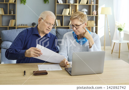 Senior couple budgeting bills with laptop and calculator at home, planning finances Senior couple budgeting bills with laptop and calculator at home, planning finances 142892742