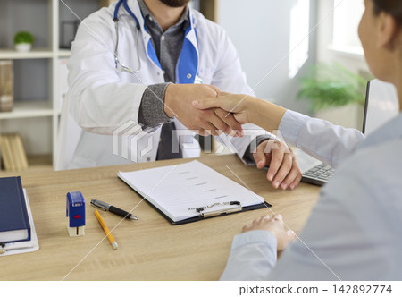 Handshake of doctor with stethoscope and woman at desk at hospital consultation Handshake of doctor with stethoscope and woman at desk at hospital consultation 142892774