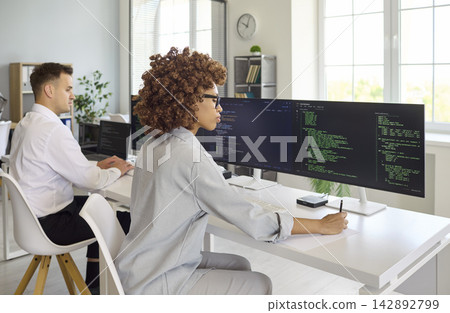 Female developer coding at multi monitor setup in contemporary collaborative office 142892799
