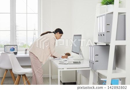 Female auditor analyzing paperwork at desktop computer in bright modern office Female auditor analyzing paperwork at desktop computer in bright modern office 142892802