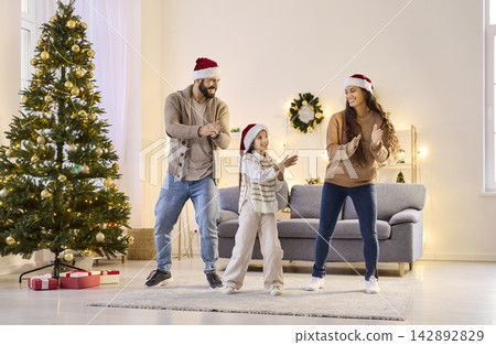 Happy family dancing with daughter at home on Christmas, wearing Santa hats 142892829
