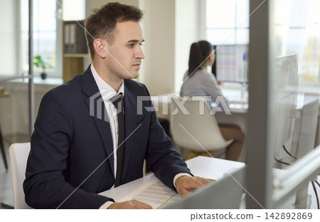 Focused businessman working at computer in office, coworker in background Focused businessman working at computer in office, coworker in background 142892869